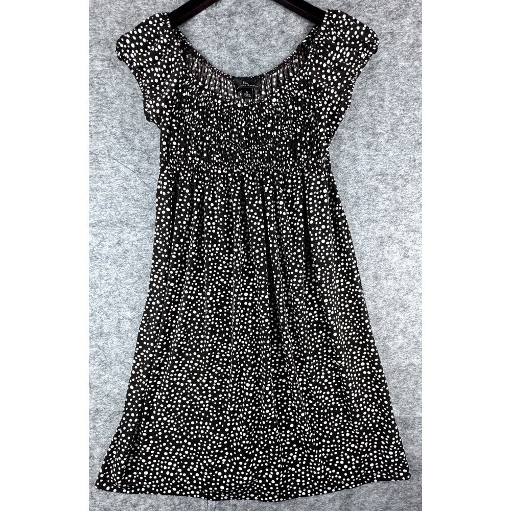 A black short-sleeve babydoll dress with an all-over white ditsy floral print, shown hanging on a black hanger against a textured gray background.