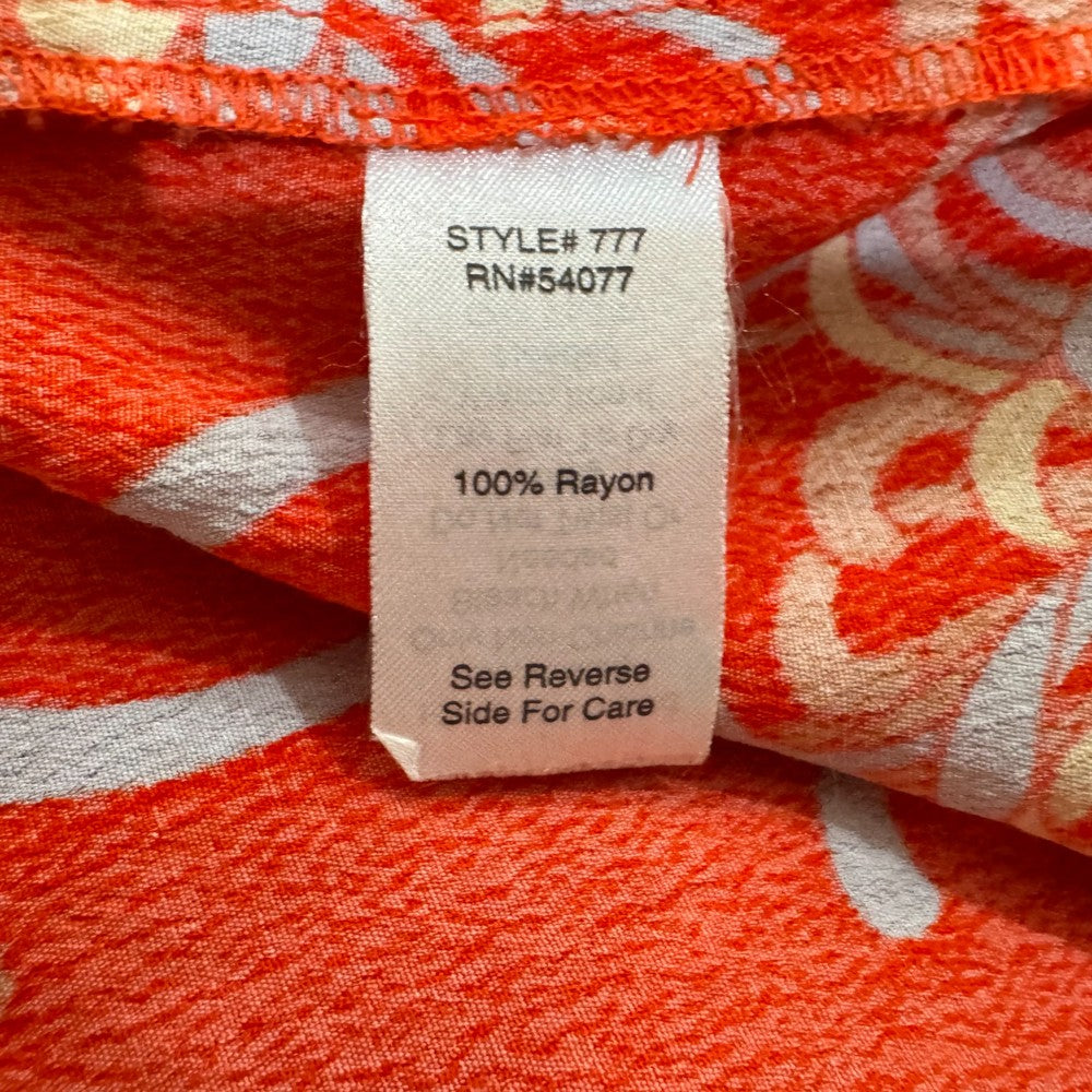 Clothing material tag of a Cabi top on a red floral patterned fabric