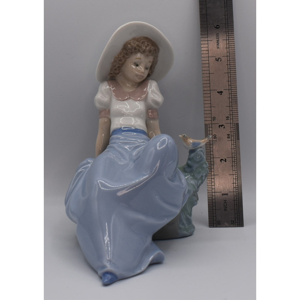 Height view of Lladro porcelain figurine of a woman with a long skirt and hat next to a ruler for scale