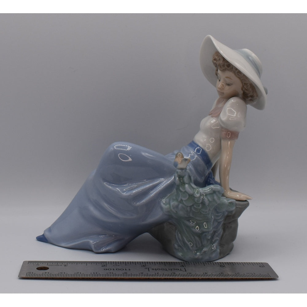 Left view of Lladro porcelain figurine of a woman in a blue dress and white hat and ruler for width