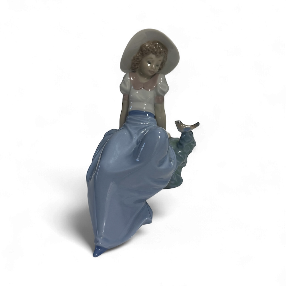 Main view Lladro porcelain figurine of a girl in a blue dress and white hat sitting on a rock with a butterfly.