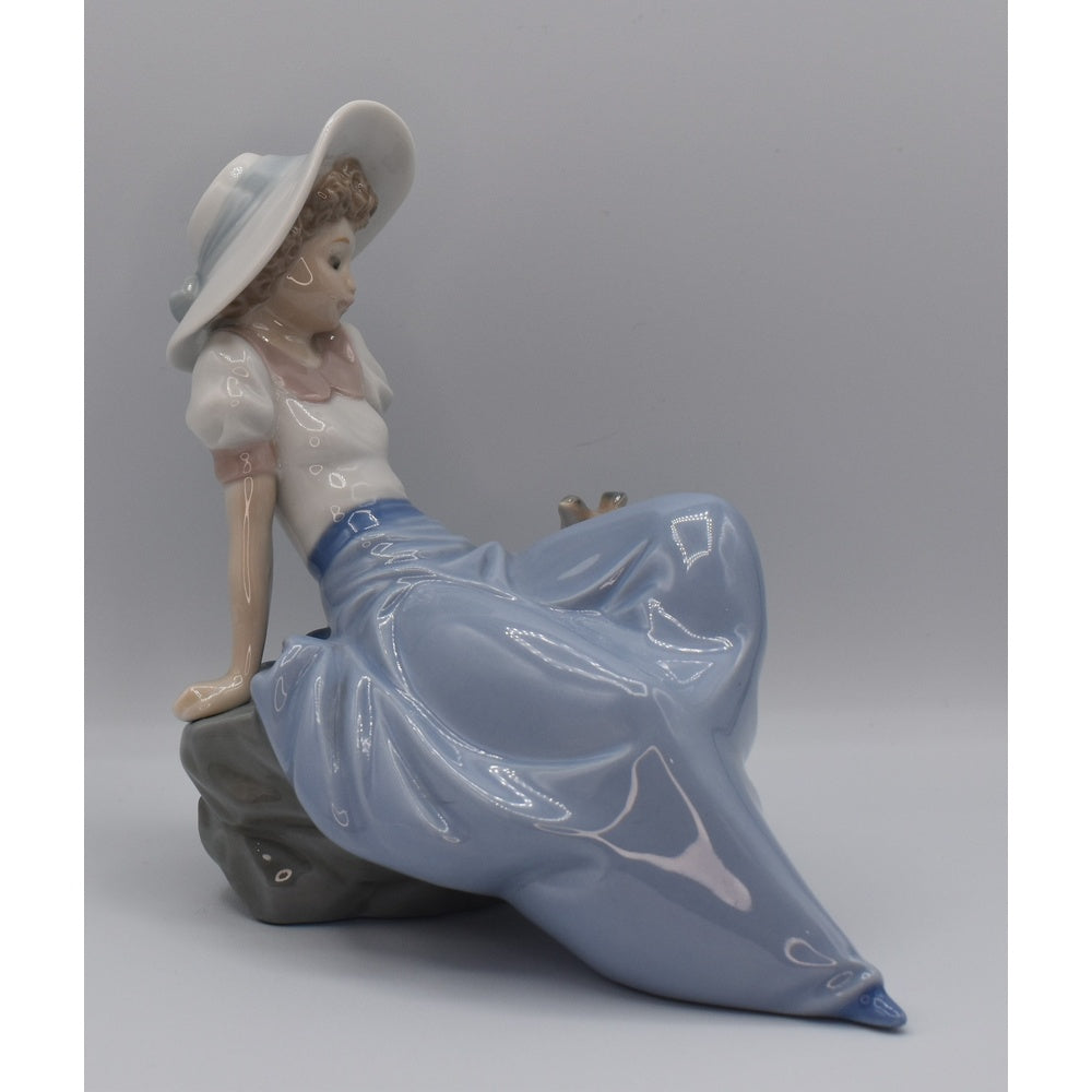 Right side view of Lladro Porcelain figurine of a woman sitting on a bench with a gray background