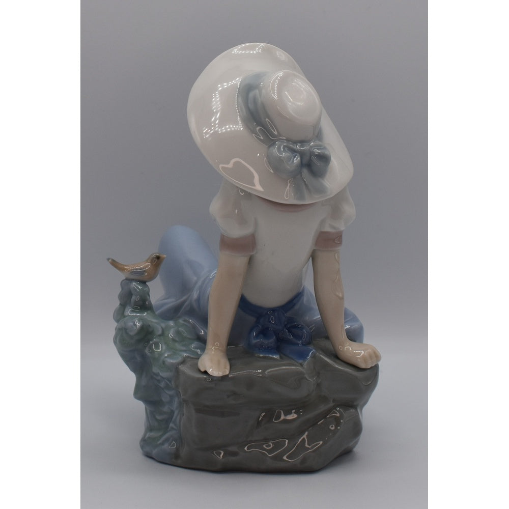 Back view of Lladro porcelain figurine of a girl with a sun hat and a bird on a gray background
