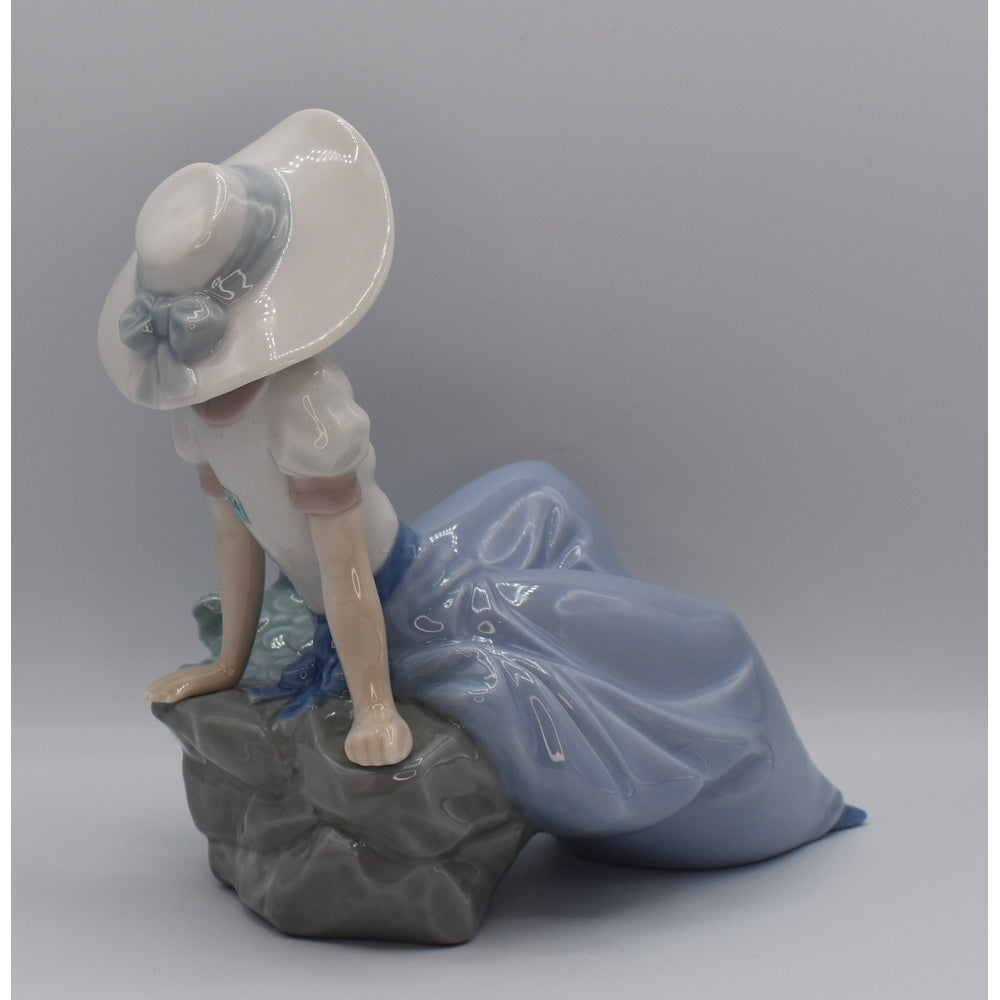 Right back view of Lladro porcelain figurine of a woman in a blue dress and white hat on a gray background