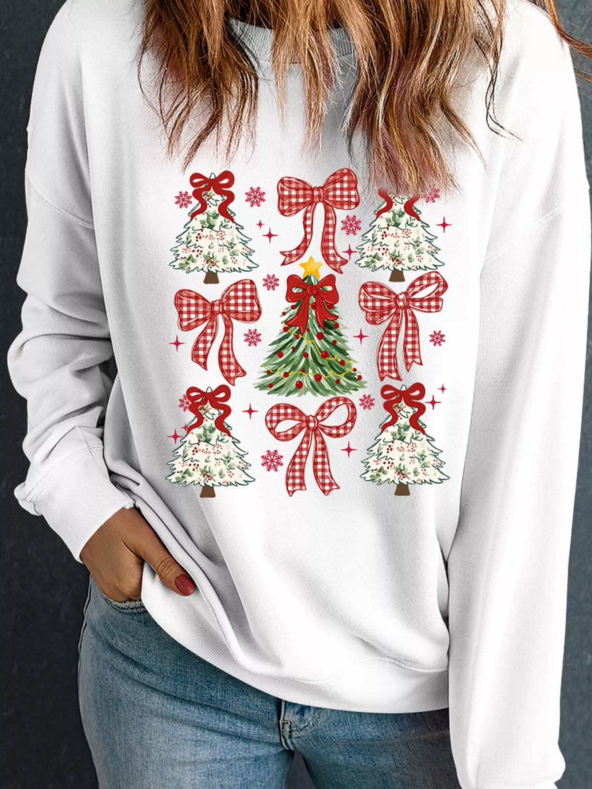 Woman wearing a white Simply Love Christmas sweatshirt with red ribbon bows and green Christmas tree prints, styled with blue jeans.