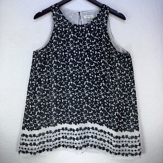 A sleeveless black and white patterned top hanging on a black hanger against a white wall. The top features an all-over small floral print and a textured, fringed-like border along the hem.