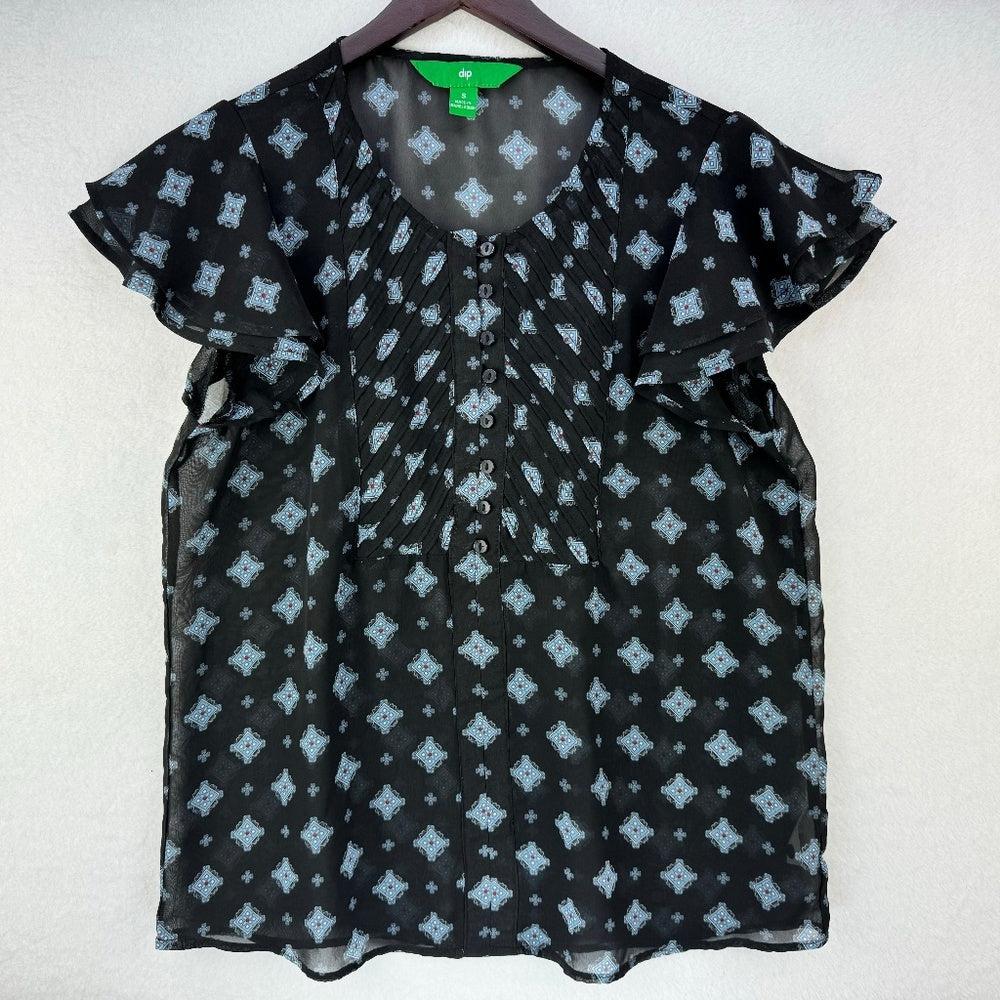 A black short-sleeve blouse with a light blue geometric pattern, displayed on a hanger against a light gray textured wall.