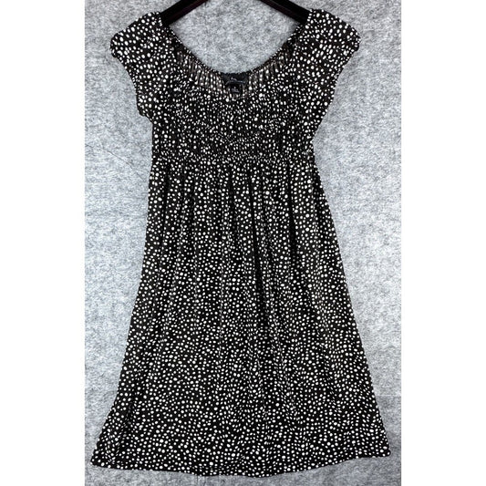 A black short-sleeve babydoll dress with an all-over white ditsy floral print, shown hanging on a black hanger against a textured gray background.