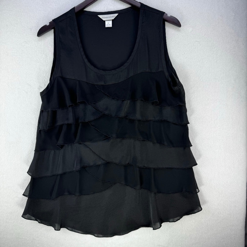 A black sleeveless tiered ruffle blouse hanging on a dark hanger against a light gray textured wall.