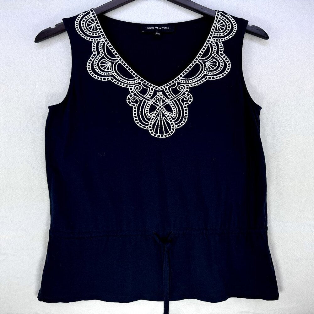 A sleeveless navy blue top hanging on a black hanger against a light textured wall. The top features a wide, ornate white embroidered yoke with a V-neckline and a drawstring detail at the waist.