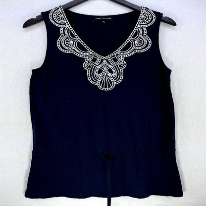 A sleeveless navy blue top hanging on a black hanger against a light textured wall. The top features a wide, ornate white embroidered yoke with a V-neckline and a drawstring detail at the waist.