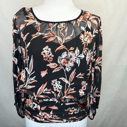 A black sheer long-sleeve blouse with a floral print in peach, orange, and white, displayed on a white mannequin torso against a light gray fabric backdrop.