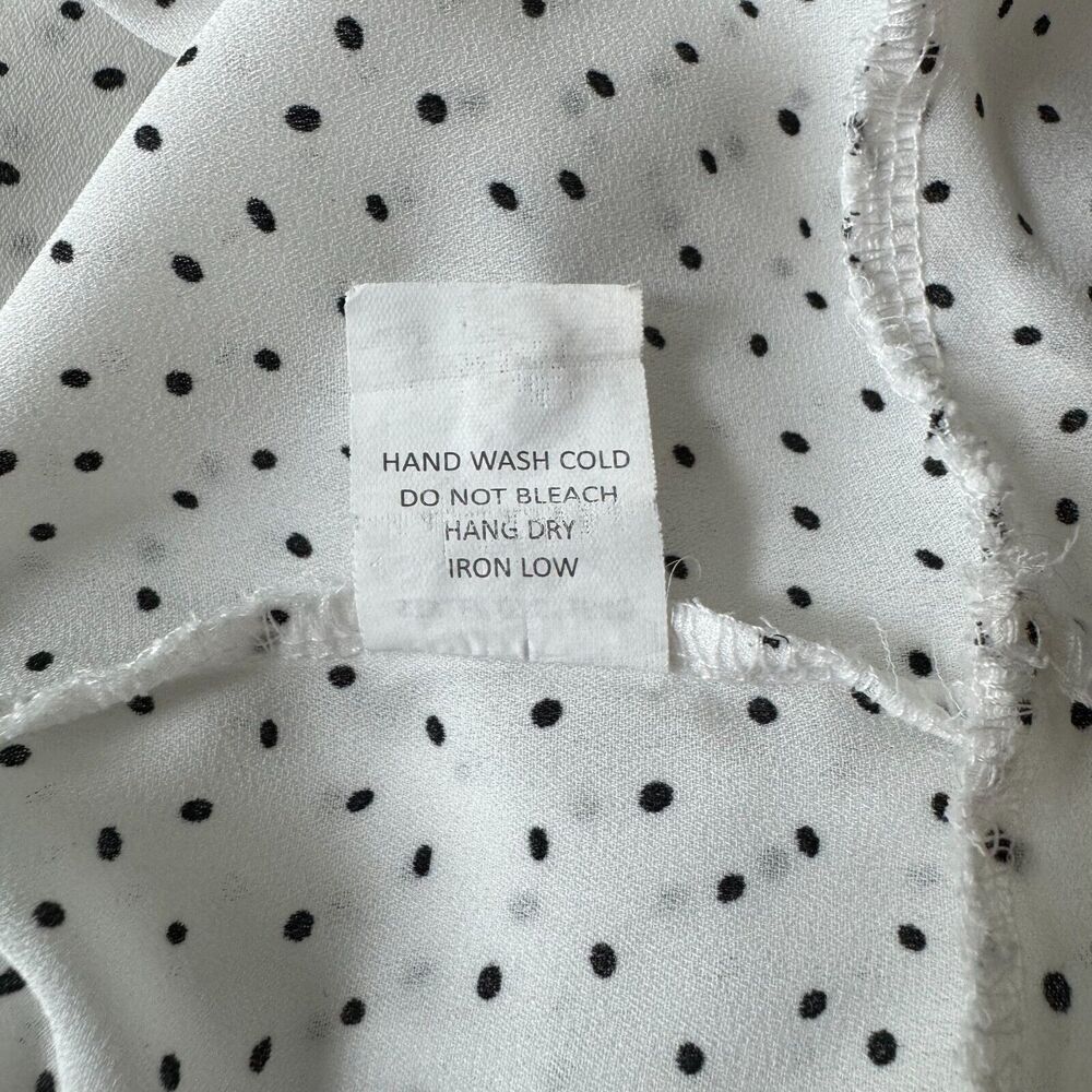 Close-up of a white fabric item with black polka dots and a sewn-in care label reading 'HAND WASH COLD DO NOT BLEACH HANG DRY IRON LOW'.