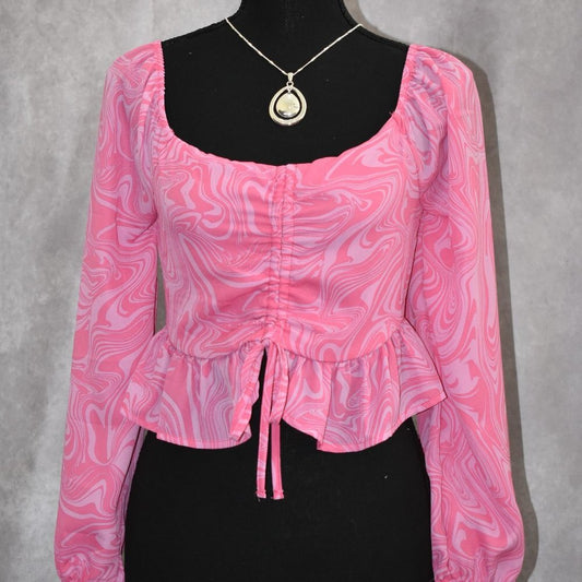 A pink and white marbled long-sleeve blouse displayed on a black mannequin torso, featuring a square neckline, gathered front, and peplum hem.