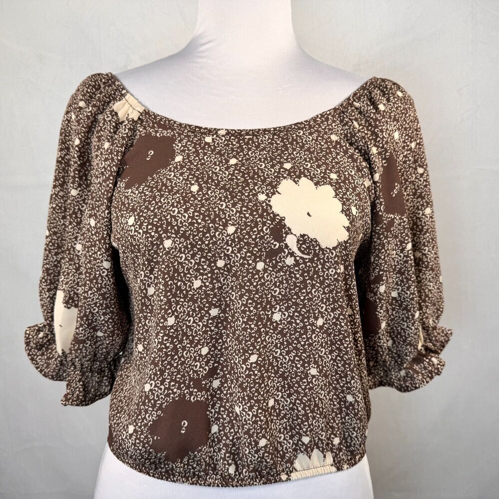A brown and beige patterned blouse with puff sleeves, displayed on a white mannequin torso against a light gray background.