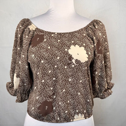 A brown and beige patterned blouse with puff sleeves, displayed on a white mannequin torso against a light gray background.
