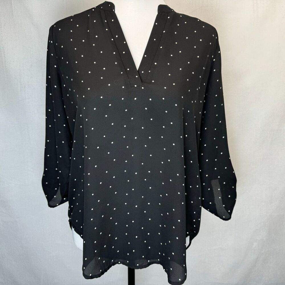 A black long-sleeve blouse with a white polka dot pattern, displayed on a white mannequin torso against a light gray fabric backdrop.