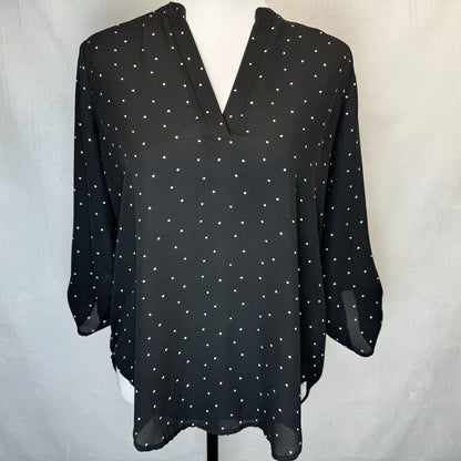 A black long-sleeve blouse with a white polka dot pattern, displayed on a white mannequin torso against a light gray fabric backdrop.
