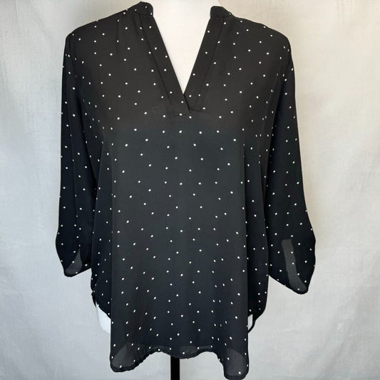 A black long-sleeve blouse with a white polka dot pattern, displayed on a white mannequin torso against a light gray fabric backdrop.