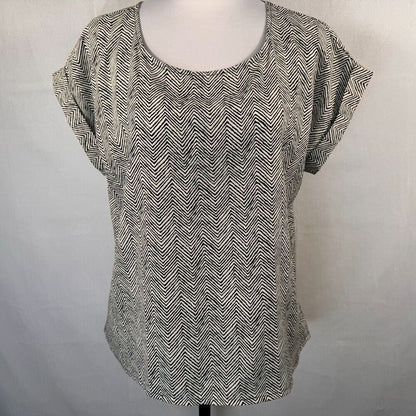 A women's short-sleeve top with a black and white chevron pattern, displayed on a mannequin torso against a light gray fabric backdrop.