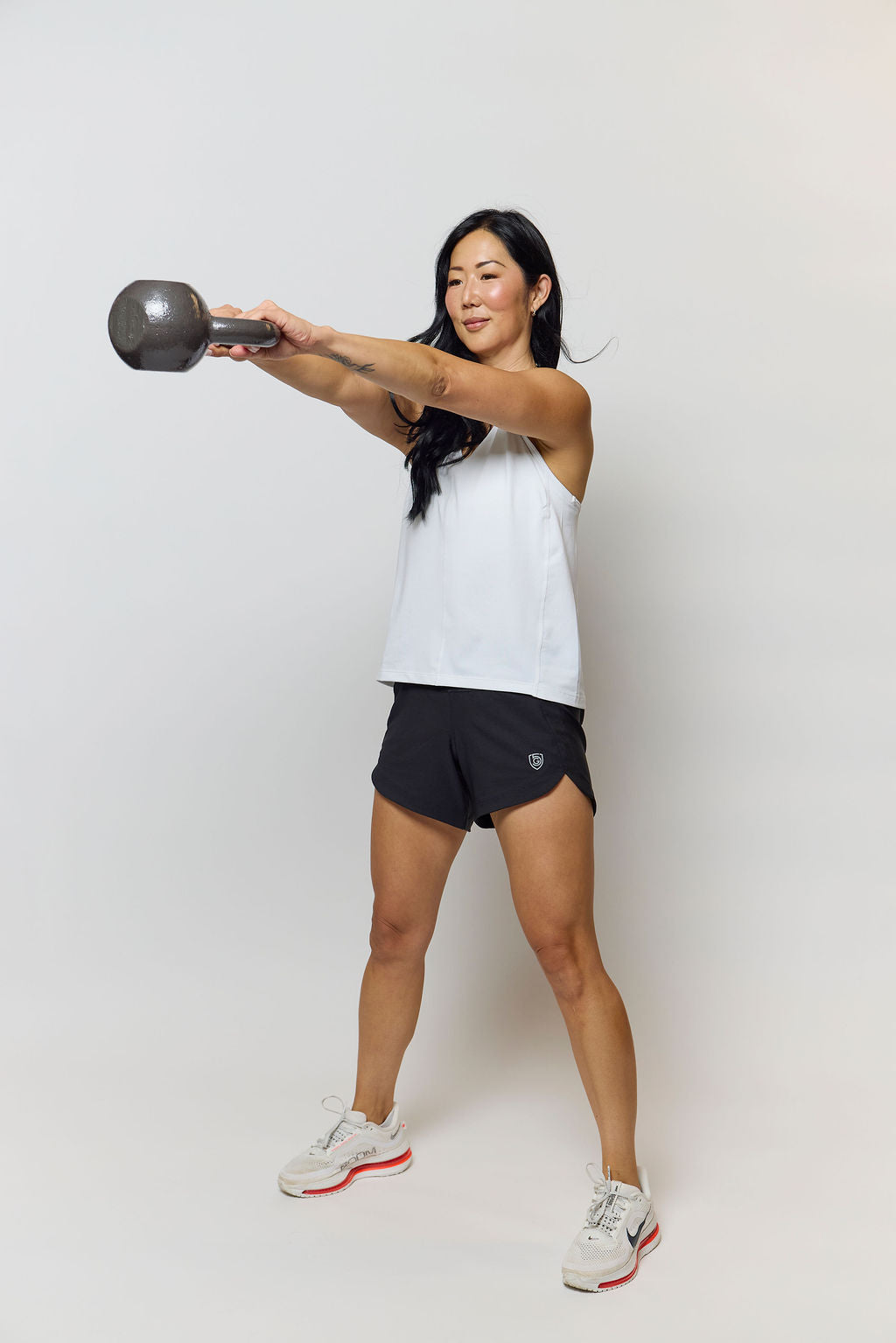 Model wearing black Goal Five Excel women's athletic workout shorts with a white sleeveless top while exercising with a dumbbell.