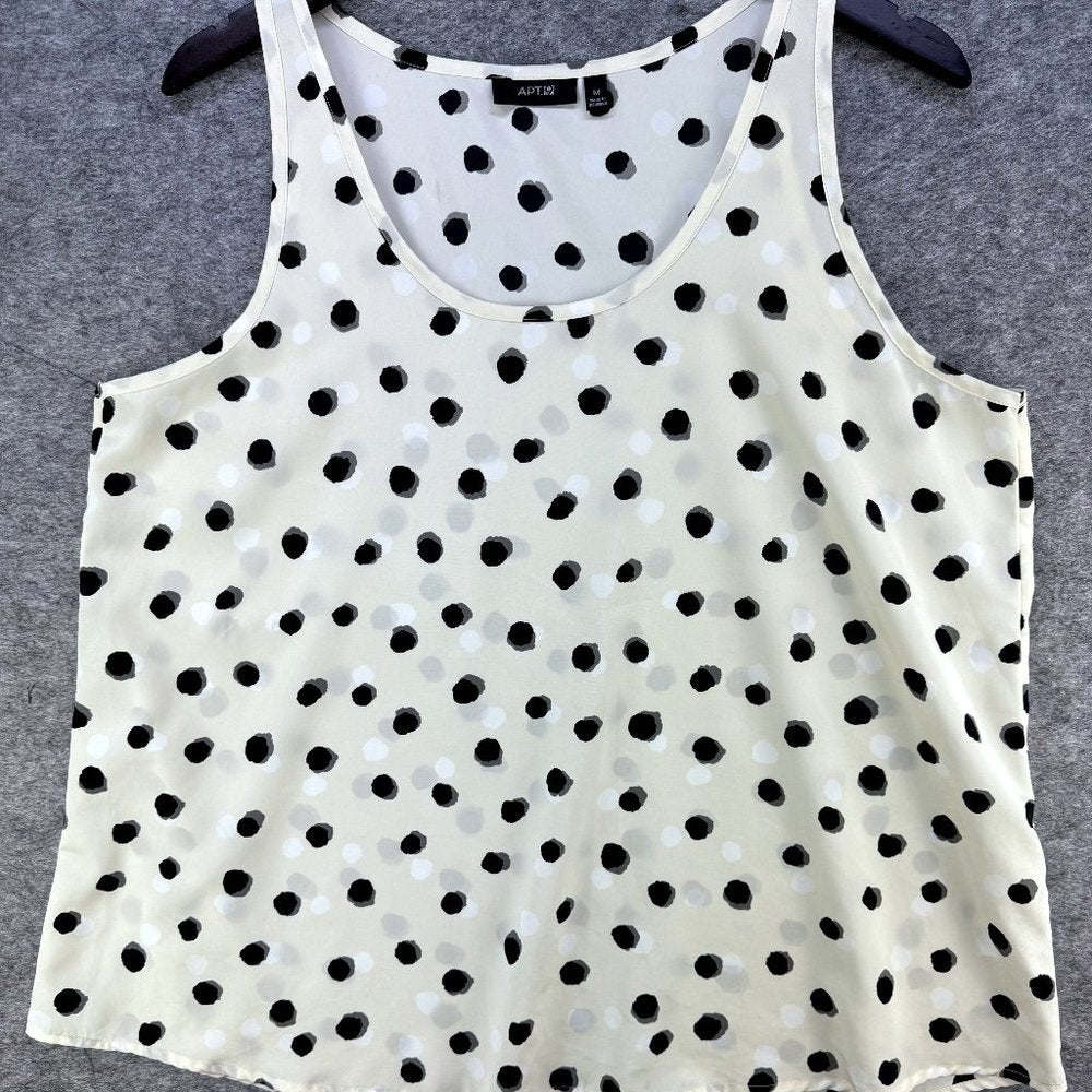 A sleeveless scoop-neck top with an all-over black and white polka dot pattern, hanging on a black hanger against a textured gray background.