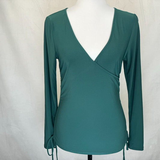 A teal green long-sleeve wrap top with a deep V-neckline, displayed on a white mannequin torso against a light gray fabric backdrop.