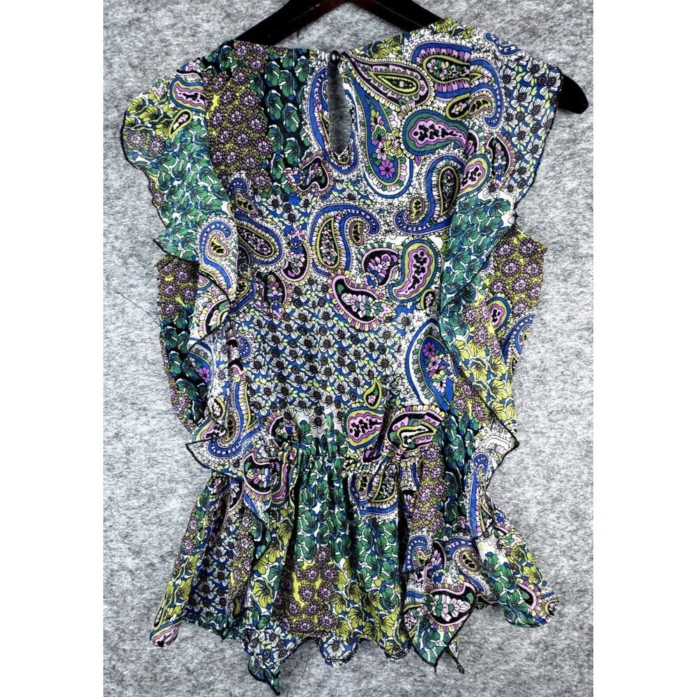 A sleeveless ruffled blouse with a vibrant paisley pattern in green, blue, purple, and yellow, hanging on a black hanger against a gray textured background.