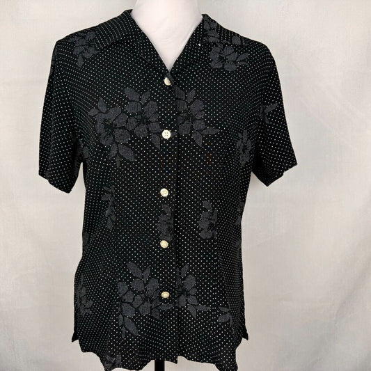 A black short-sleeve button-up blouse with a white polka dot pattern and dark gray floral lace overlay, displayed on a white mannequin torso against a light gray fabric backdrop.