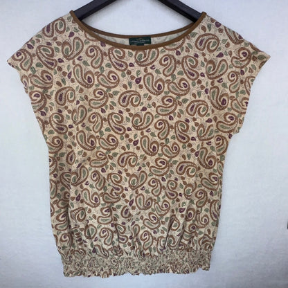 A women's short-sleeve knit top with a beige base and an all-over brown and muted green paisley pattern, hanging on a black hanger against a light gray wall.
