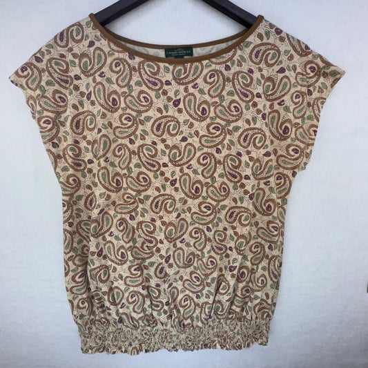 A women's short-sleeve knit top with a beige base and an all-over brown and muted green paisley pattern, hanging on a black hanger against a light gray wall.