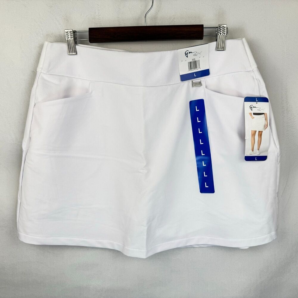 A pair of white women's shorts hanging on a dark wooden hanger against a light gray wall. The shorts feature side pockets and are shown with retail tags, including a blue size guide and a brand tag that appears to read 'G&G'.