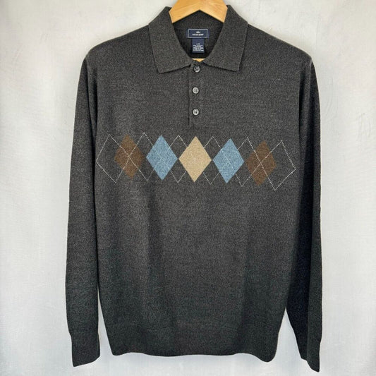 A dark gray long-sleeve knit polo sweater with an argyle diamond pattern across the chest in brown, beige, and light blue, hanging on a wooden hanger against a light gray wall.
