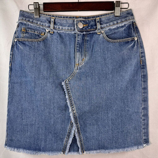 A blue denim mini skirt with a frayed hem and diagonal front slit, hanging on a dark wooden hanger against a white fabric background.