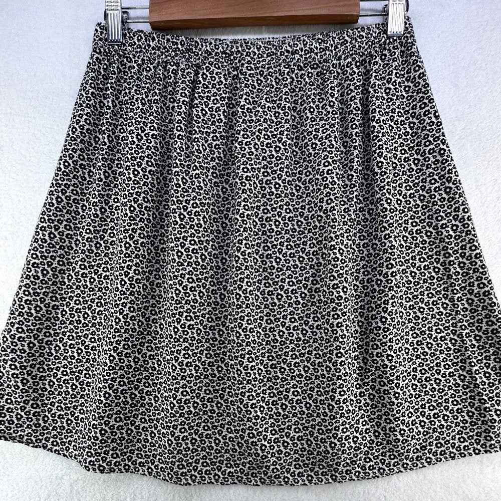 A black and white leopard print A-line skirt hanging on a wooden hanger against a white textured background.
