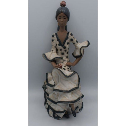 A ceramic figurine of a seated woman in a flamenco-style dress with black polka dots and black trim, set against a plain gray background.