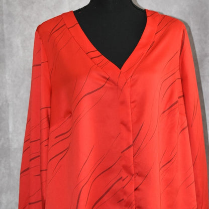 A bright red satin blouse with a black abstract line pattern, displayed on a black mannequin torso against a textured gray background.