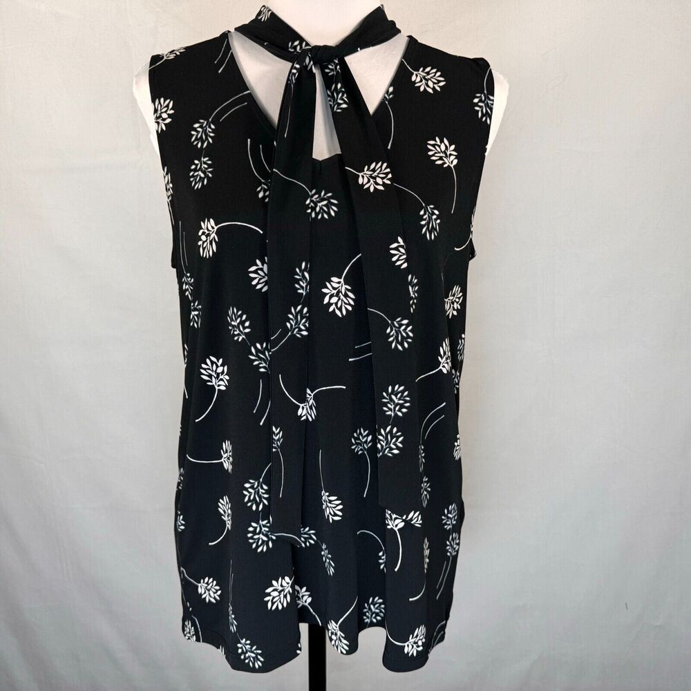 A sleeveless black blouse with a white floral vine pattern and a tie-neck detail, displayed on a white dress form against a light gray background.