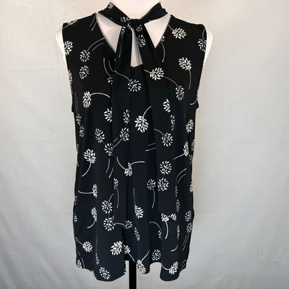 A sleeveless black blouse with a white floral vine pattern and a tie-neck detail, displayed on a white dress form against a light gray background.