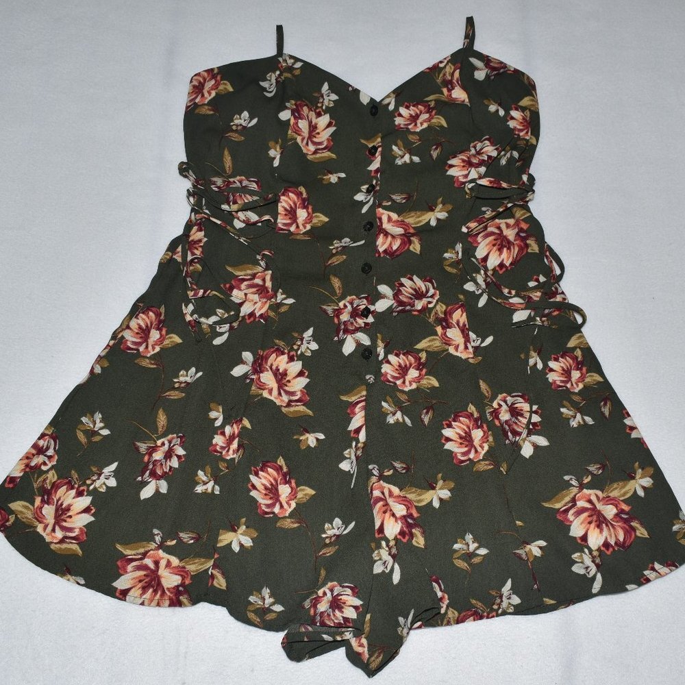 A sleeveless fit-and-flare dress with a dark olive green base and a red, pink, and white floral print, featuring a sweetheart neckline, button front, and side tie details.