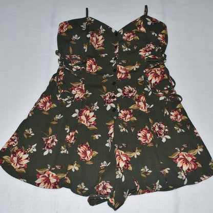 A sleeveless fit-and-flare dress with a dark olive green base and a red, pink, and white floral print, featuring a sweetheart neckline, button front, and side tie details.