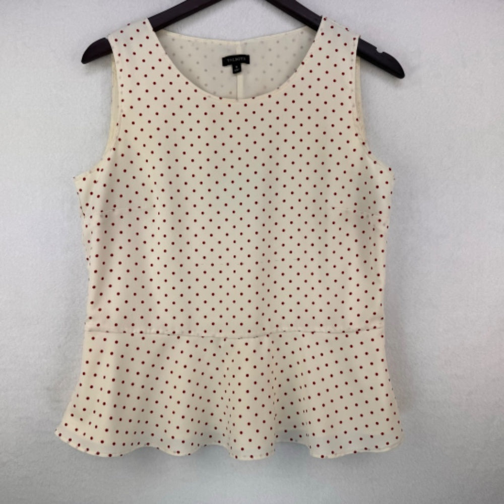 A sleeveless scoop-neck top with a small dark brown polka dot pattern on a cream base, hanging on a black hanger against a light gray textured wall.