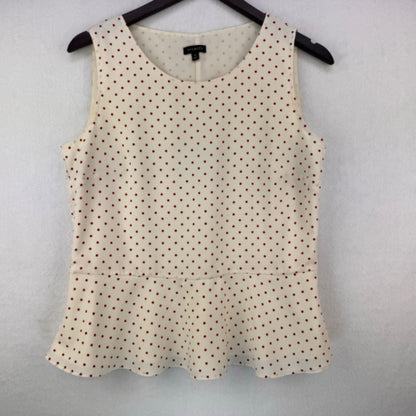A sleeveless scoop-neck top with a small dark brown polka dot pattern on a cream base, hanging on a black hanger against a light gray textured wall.