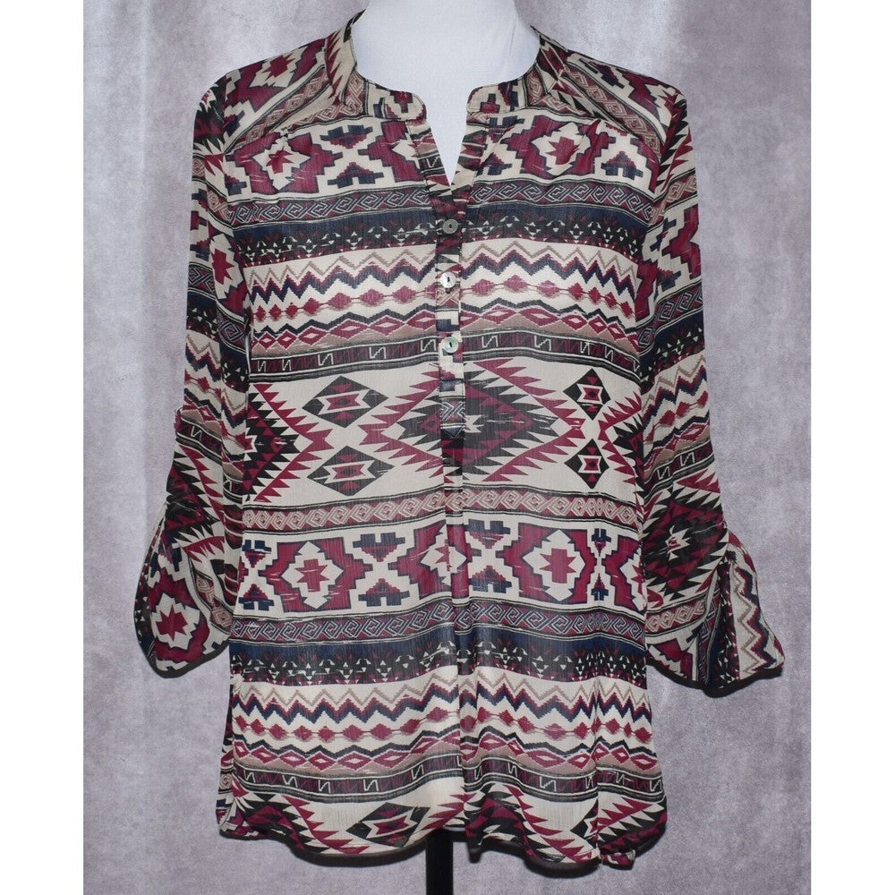 A long-sleeve button-up blouse with a colorful geometric tribal pattern, displayed on a mannequin torso against a textured gray background.
