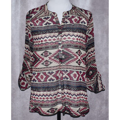 A long-sleeve button-up blouse with a colorful geometric tribal pattern, displayed on a mannequin torso against a textured gray background.