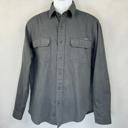 A dark gray long-sleeve button-up shirt with two chest pockets, displayed on a white mannequin torso against a light gray wall.
