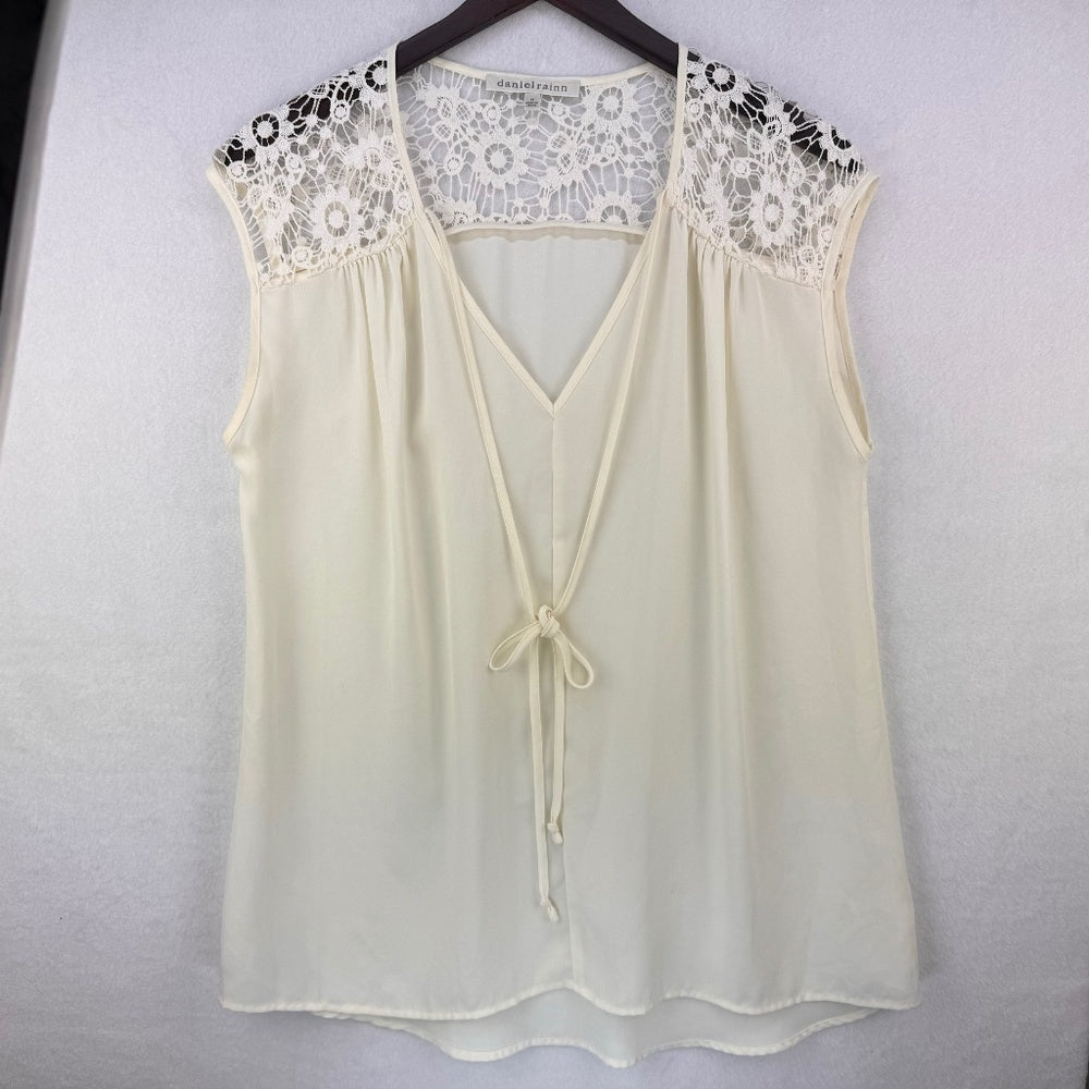 An off-white sleeveless blouse with a lace yoke and drawstring front, hanging on a dark hanger against a light textured wall.