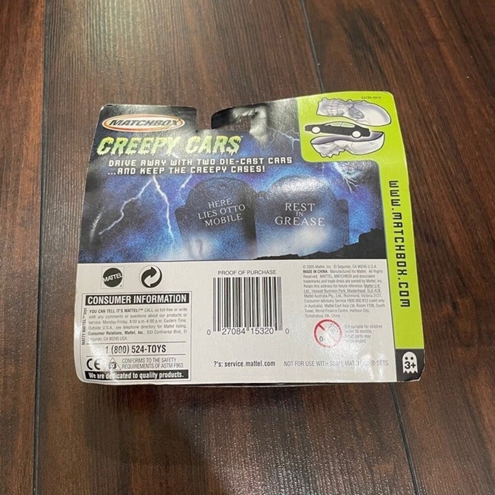 Matchbox Creepy Cars toy packaging on a dark wood floor, showing the back of the blister card with barcode, consumer information, and product imagery.
