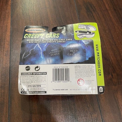 Matchbox Creepy Cars toy packaging on a dark wood floor, showing the back of the blister card with barcode, consumer information, and product imagery.