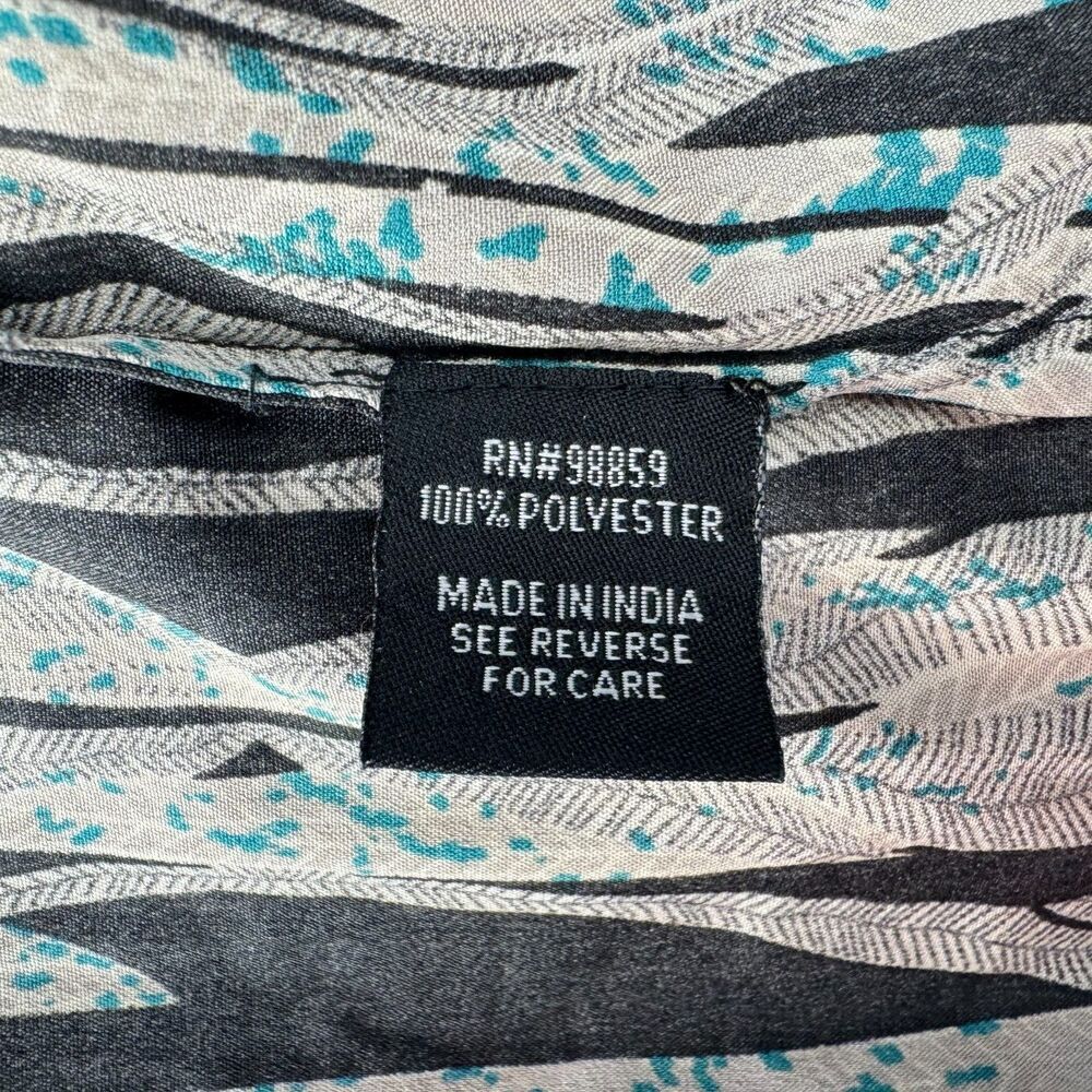 Close-up of a garment's interior neck label reading 'RN#98859 100% POLYESTER MADE IN INDIA SEE REVERSE FOR CARE' on a black patch, with a gray, white, and turquoise abstract patterned fabric visible around it.